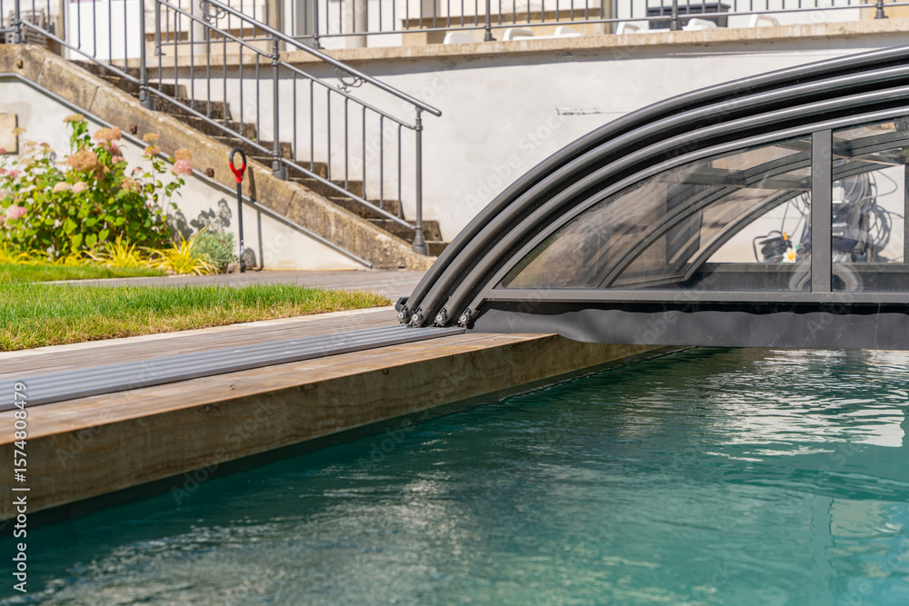 Fototapeta premium Vue d’une piscine couverte entourée d’un caillebotis en bois, intégrée harmonieusement dans un jardin paysager conçu par une entreprise spécialisée.