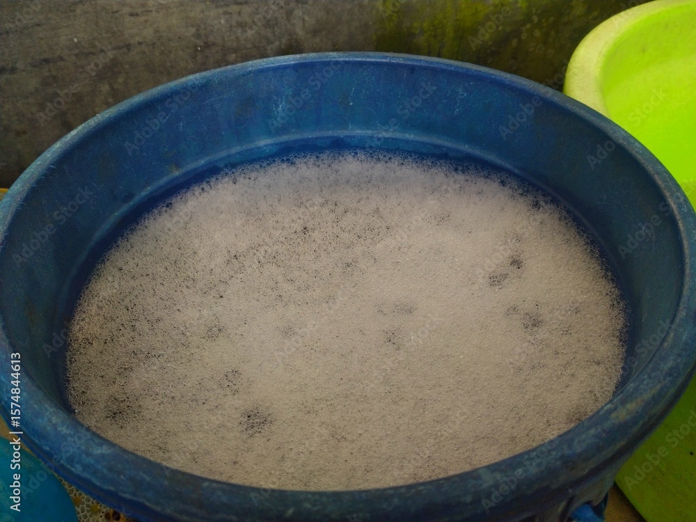 A blue plastic bucket filled with white soap suds and water, ready for washing or cleaning. A blue plastic bucket filled with white soap suds and water, ready for washing or cleaning.