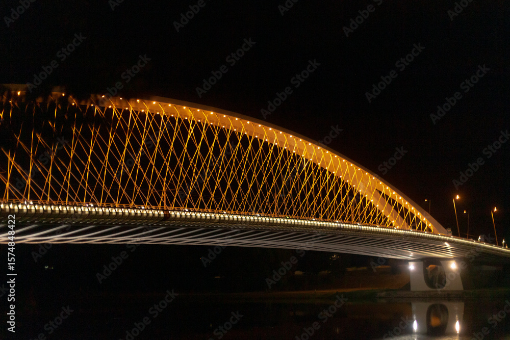 Obraz premium The stunning night view of a beautifully lit bridge is highlighted, showcasing its incredible architectural design, along with light trails created by the passing vehicles nearby