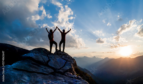 Foto At sunset, two mountain climbers pose on a rock at the summit, raising their arms in joy at their success