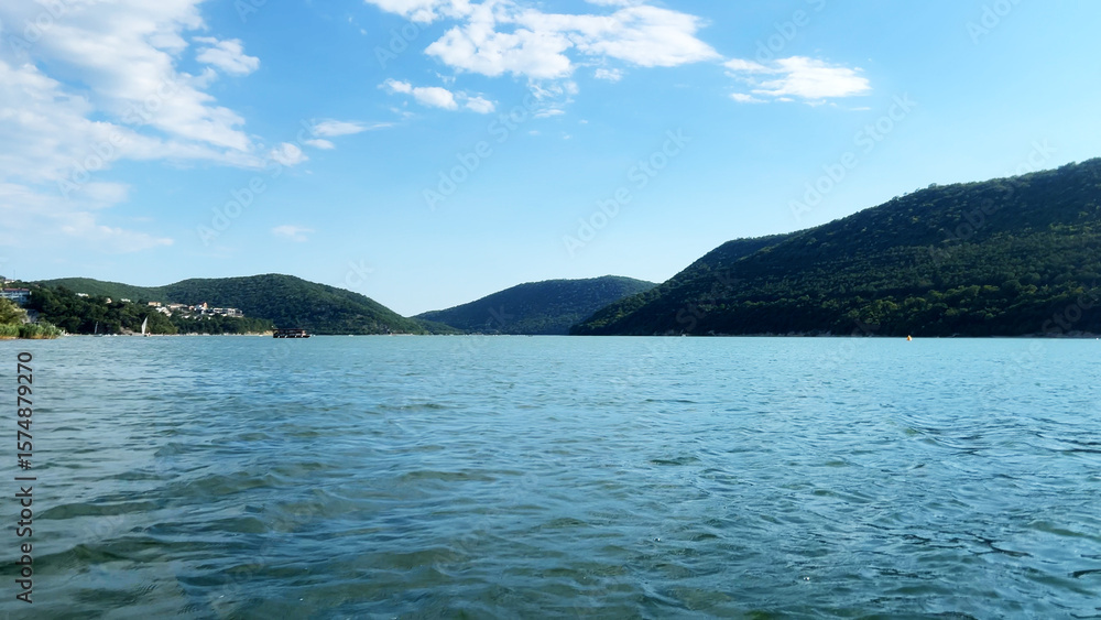 Serene landscape featuring calm blue water reflecting the sky, surrounded by lush green hills under a bright sunny day, creating a peaceful natural environment Serene landscape featuring calm blue water reflecting the sky, surrounded by lush green hills under a bright sunny day, creating a peaceful natural environment