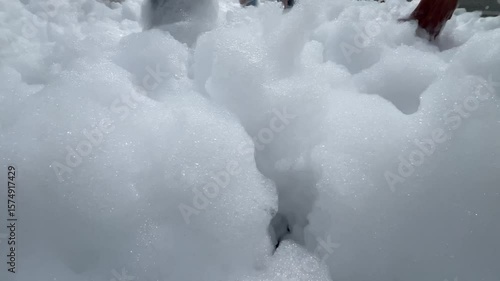 Children's feet are running on the beach in foam. White foam for a foam party. The beach is covered with a layer of foam or bubbles formed from the foam.A holiday on vacation.High quality 4k footage