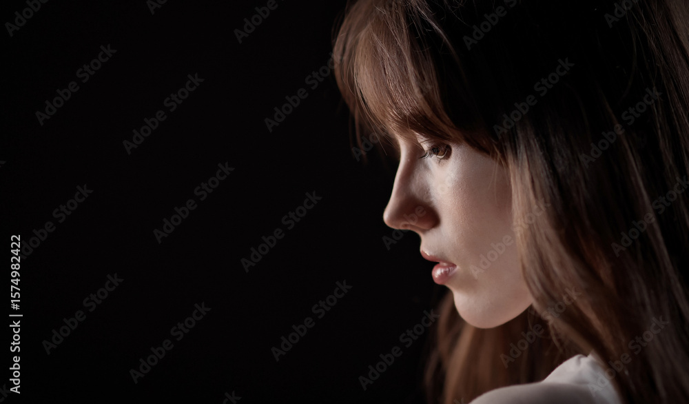 Fototapeta premium Profile of a beautiful young woman with long brown hair looking down, isolated on a black background