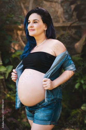 pregnant woman with exposed belly, colored hair, outdoors in jeans and black top.