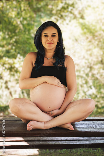 pregnant woman with exposed belly, colored hair, outdoors in a black top with trees in the background.