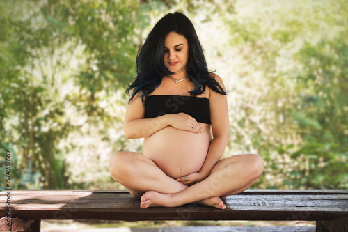 pregnant woman with exposed belly, colored hair, outdoors in a black top with trees in the background.