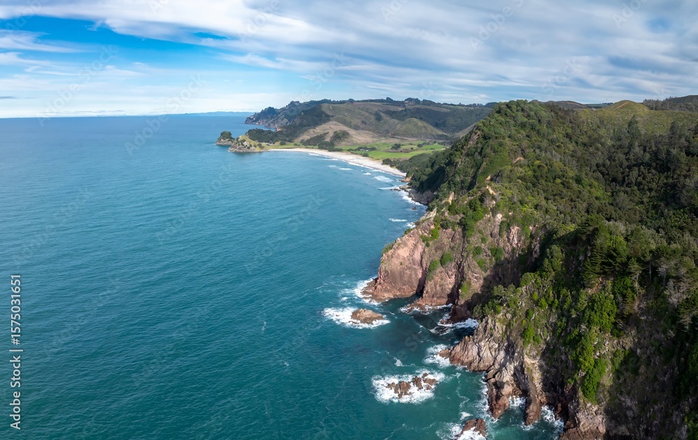 Fototapeta premium Aerial view of the coastline in Whiritoa, Coromandel Peninsula, New Zealand. The turquoise ocean water meets the rocky cliffs and sandy beach, showcasing the natural beauty of the landscape.