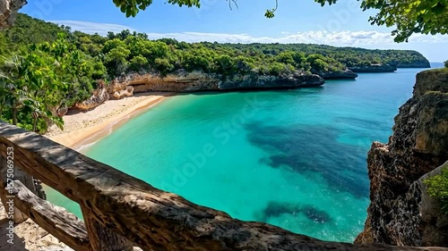 Scenic aerial view of a tropical beach with turquoise water and lush greenery viewed from a wooden railing in daylight. The frame features a stunning panorama of the sandy shore, vibrant ocean, and