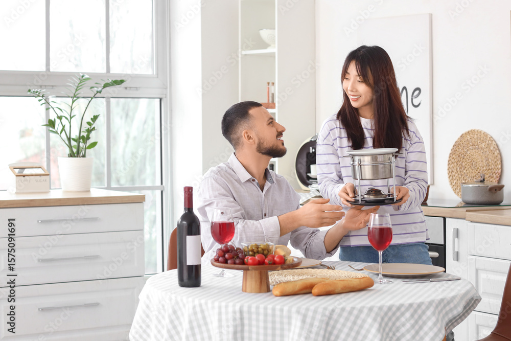 Young happy woman bringing cheese fondue for snacks and glasses of wine to her boyfriend at home Young happy woman bringing cheese fondue for snacks and glasses of wine to her boyfriend at home