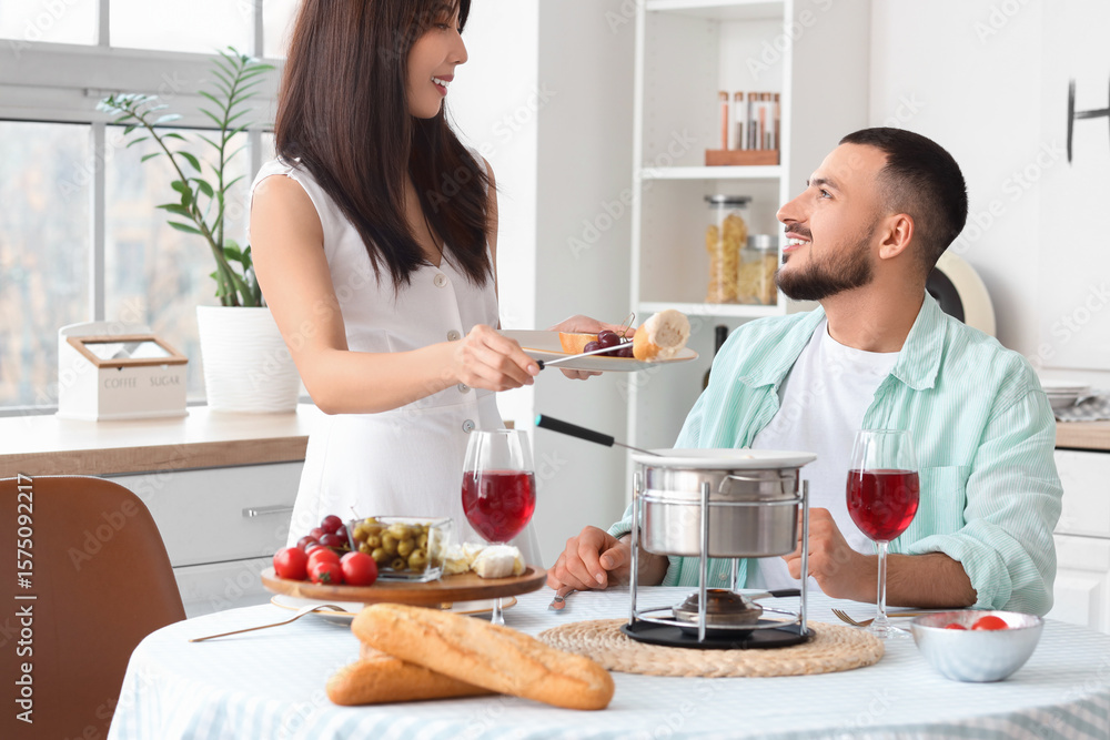 Young happy couple with glasses of wine dipping croutons into cheese fondue at home Young happy couple with glasses of wine dipping croutons into cheese fondue at home