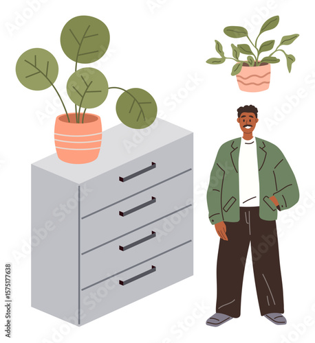Young man in casual attire stands near a four-drawer cabinet with potted plants. Ideal for interior design, home organization, casual style, workplace decor, indoor gardening, self-expression, simple