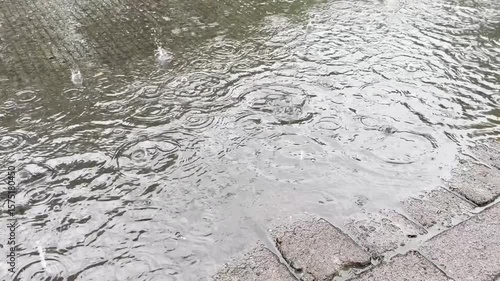 Rain drops creating ripples and circles on a dark, wet surface with brick edge, abstract.