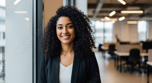 Confident Young  Businesswoman with Curly Hair Smiling in Modern Office Setting.