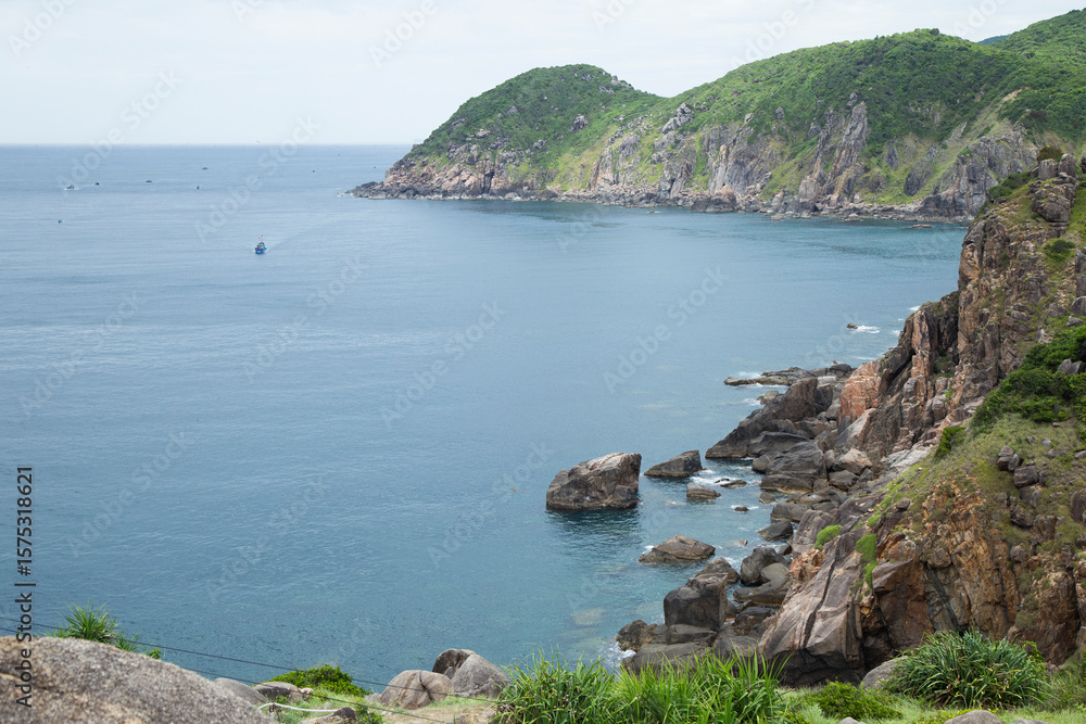 Fototapeta premium A lone boat drifts in the distance, emphasizing the vastness and tranquility of this natural Vietnamese seascape. Peace, isolation, and the enduring beauty of untouched coastal environments.