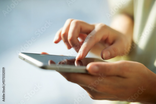 スマホを操作する女性の手元　A close-up of a woman's hands operating a smartphone　Generative AI