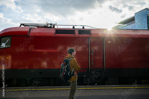 Photography Man with backpack standing on train platform with red train
