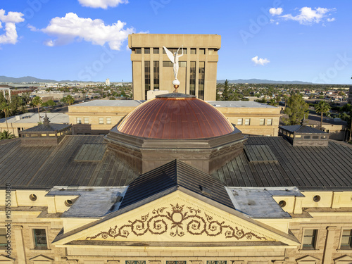 Aerial view of the copper dome of the Arizona State Capitol building gleams beneath a bright sky, flanked by modern architecture, Phoenix, Arizona, United States.