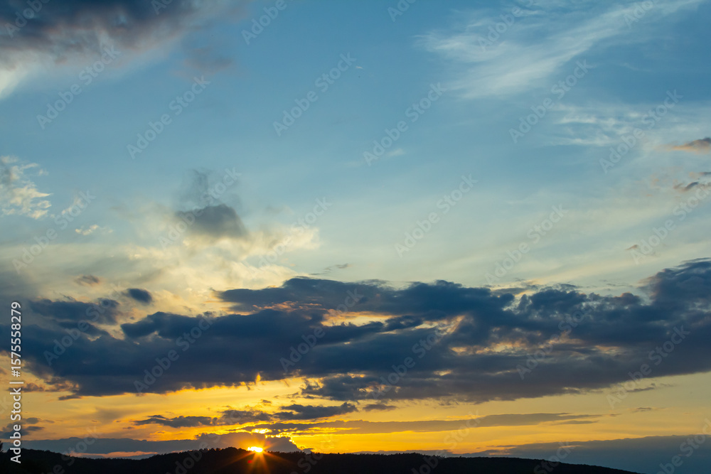Fototapeta premium Vibrant sunset over rolling hills with dramatic clouds illuminating the evening sky and casting warm colors