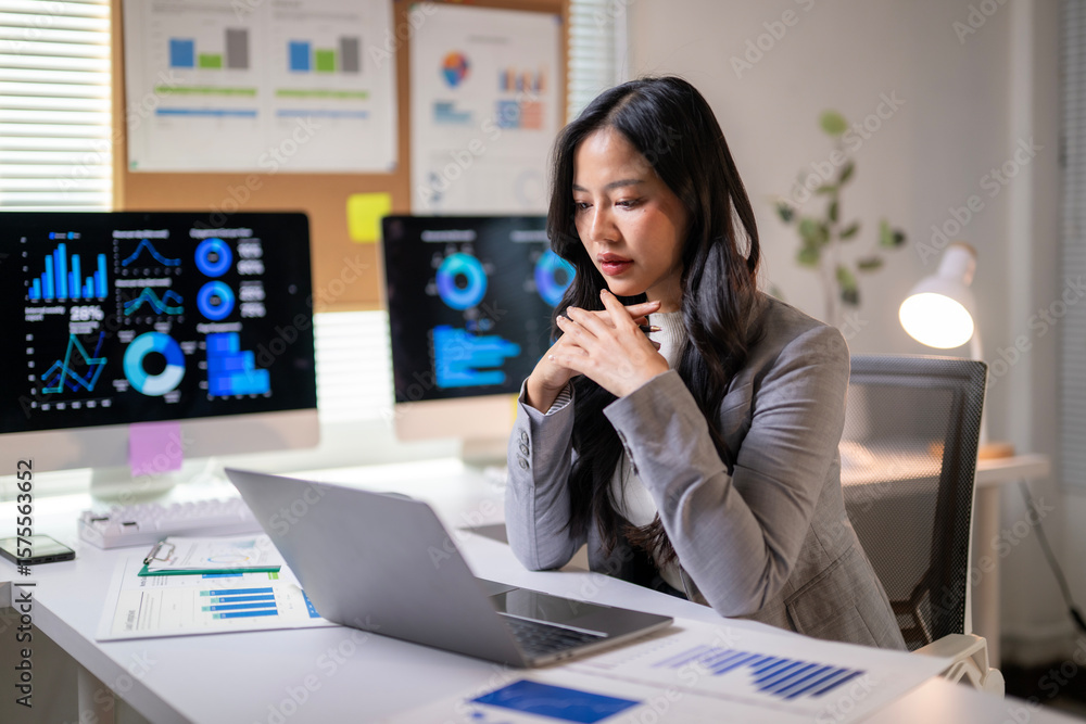 Obraz premium A woman is sitting at a desk with a laptop and a stack of papers