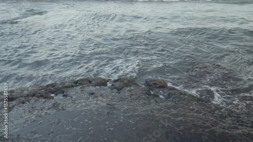 Closeup shot of foams created by the ocean waves meet a rocky shoreline.