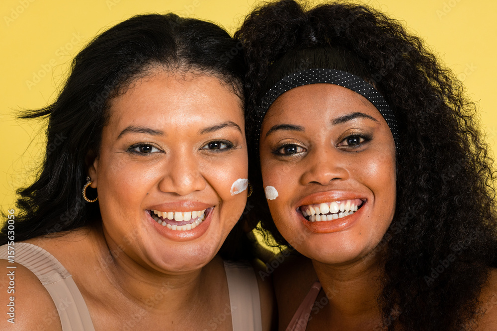 Diverse female friends standing in studio showing cream dollops on cheeks with dotted headband Diverse female friends standing in studio showing cream dollops on cheeks with dotted headband