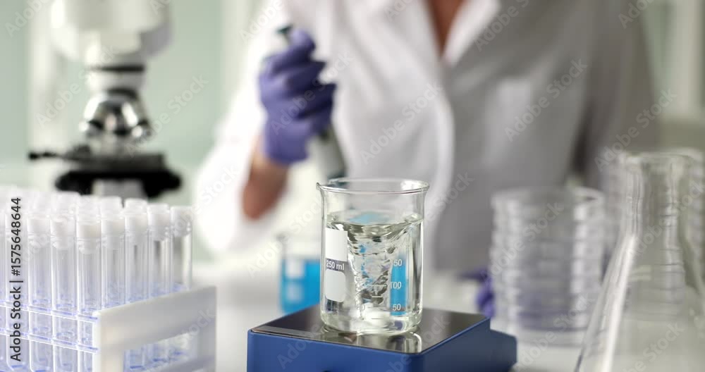 Scientist in lab coat operates pipette near swirling liquid in beaker. Vortex spins rapidly creating dynamic motion during chemical experiment Scientist in lab coat operates pipette near swirling liquid in beaker. Vortex spins rapidly creating dynamic motion during chemical experiment