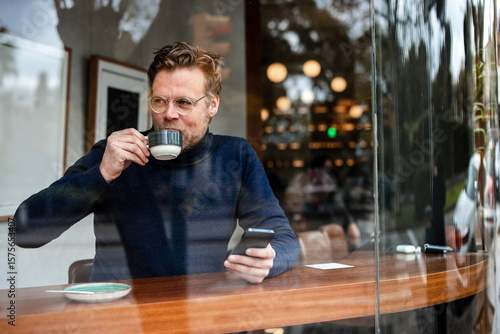 Businessman with smart phone drinking coffee in cafe