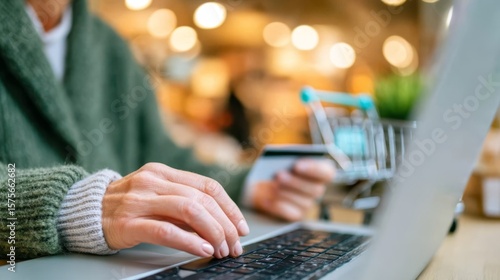 A person uses a laptop and holds a credit card, suggesting online shopping or digital payment in a cozy, softly lit environment.