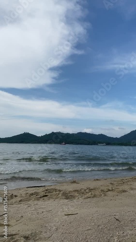 The scene shows tranquil water with small boats, backed by distant green hills and a cloudy blue sky.