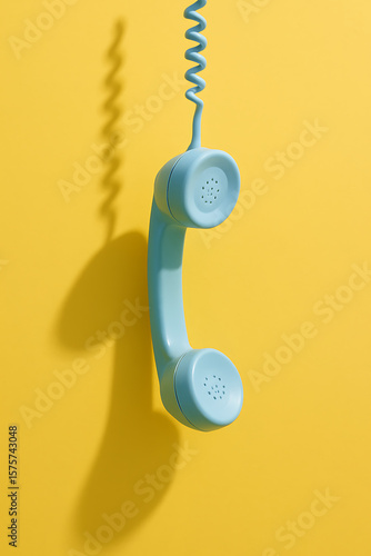 Blue vintage telephone hanging against a bright yellow background creating a bold visual contrast