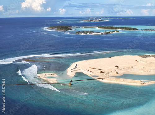 Aerial view of turquoise waters meet sandy shores, where land reclamation reshapes the island's edge under a vast sky, Gulhi, Kaafu Atoll, Maldives.