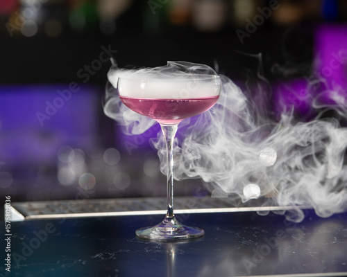 This visually striking pink alcoholic cocktail in a coupe glass features a large with more smoke billowing around it