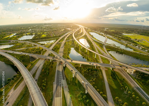 Aerial view of a complex interchange of roads and highways reflecting the sunset, cutting through the lush green landscape, Sunrise, Florida, United States.