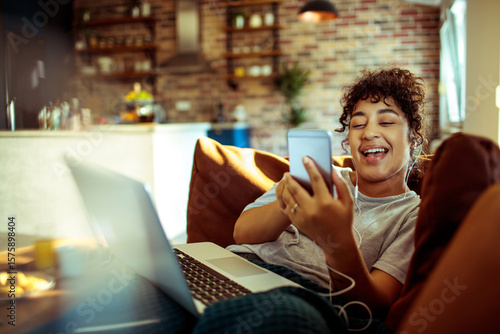 Happy woman listening to music with earphones on phone while relaxing at home