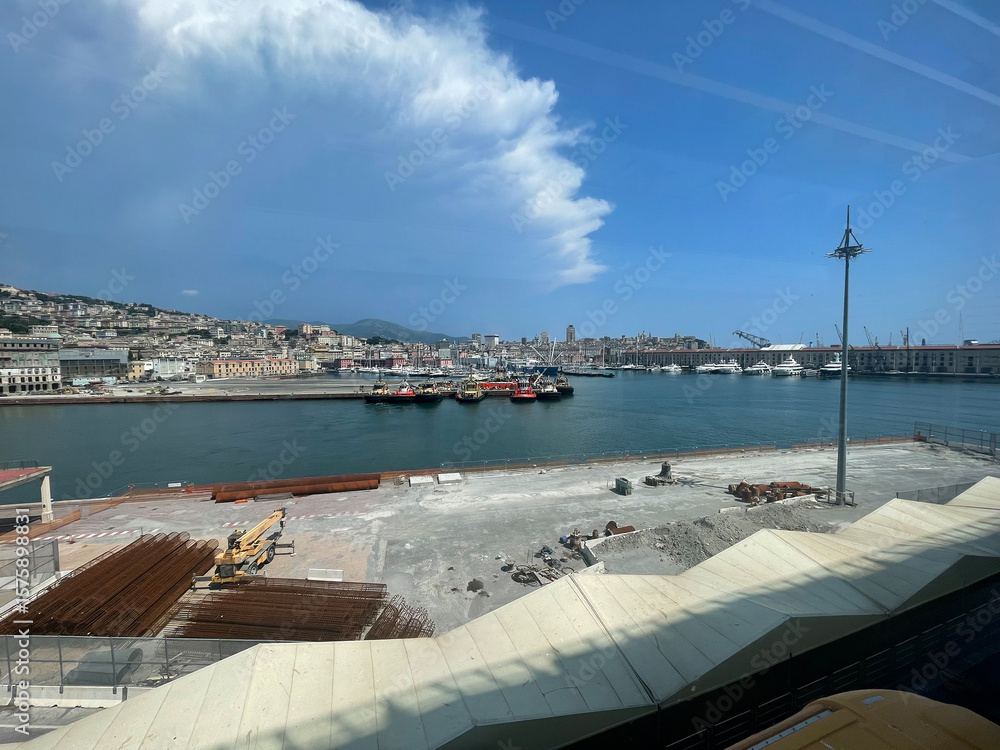 Fototapeta premium Panoramic view of the harbor of Genoa, Italy, with colorful historic buildings, construction materials on the quay, several tugboats moored in the port, and hills with residential houses