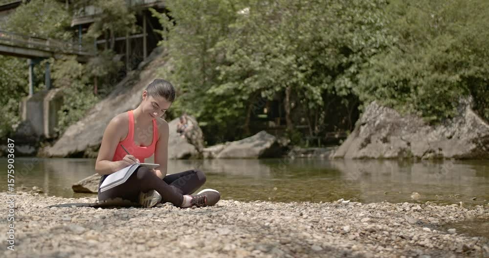 Young woman takes a moment to journal by the river after yoga and stretching. She is enjoying the peace and quiet of nature. Young woman takes a moment to journal by the river after yoga and stretching. She is enjoying the peace and quiet of nature.