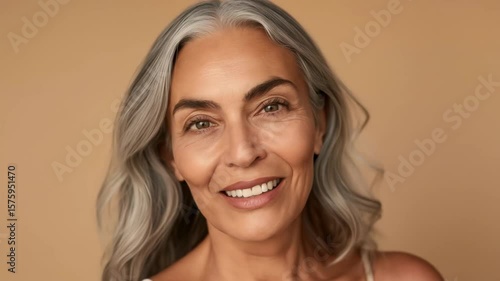 Headshot portrait of a happy, beautiful elderly woman with natural gray hair smiling, looking at camera.