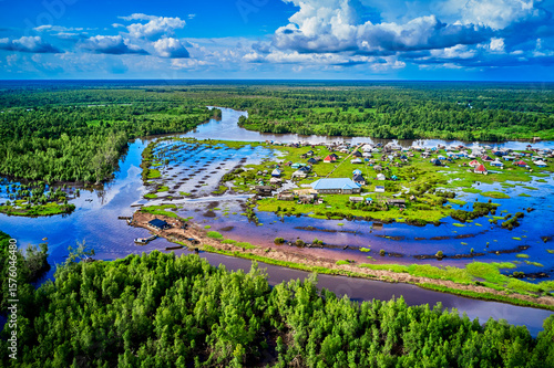 Aerial view of a riverine community nestled amidst a vibrant green forest, with waterways reflecting the azure sky above, Opuama, Delta, Nigeria.