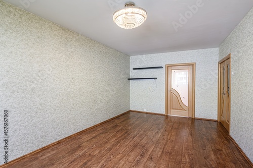 room featuring wooden floors, patterned wallpaper, and a decorative chandelier. Two wooden doors and shelves add to the interior design