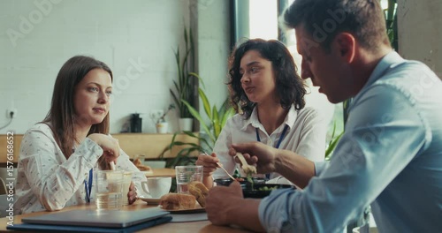 Three caucasian intern teammates enjoy lunch together in slow motion at bright sunny office cafeteria