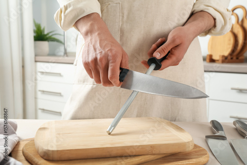 Obraz na płótnie Man sharpening knife with sharpener at beige table indoors, closeup