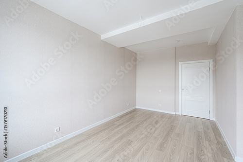 bright, empty room features light wood flooring, neutral walls, a white door, and a clean, minimalist aesthetic