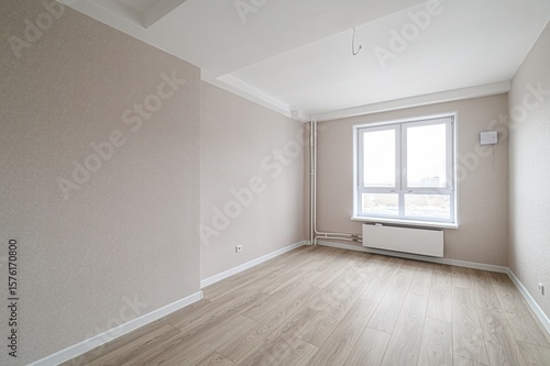 Empty room with beige walls, light wood floor, and a window. The room is bright and appears newly renovated or in the process of being finished
