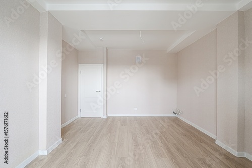 Fotografija bright, empty room with light-colored wooden floors, neutral walls, a white door, and a layered ceiling