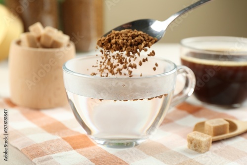 Картината върху платно Putting instant coffee into cup at light table, closeup