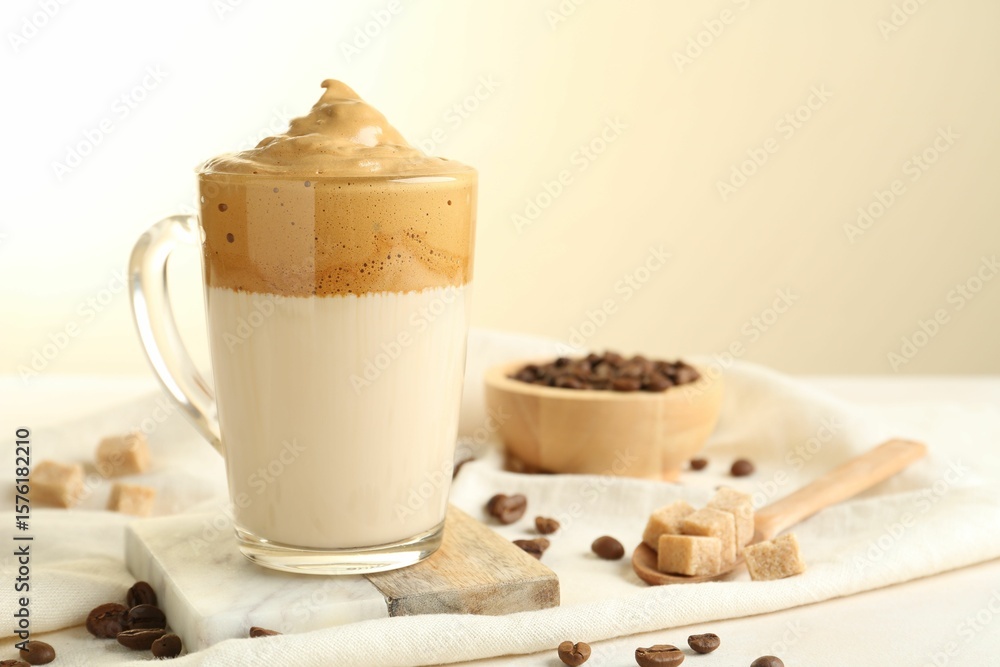 Obraz premium Delicious dalgona coffee in glass cup, beans and brown sugar on light table, closeup