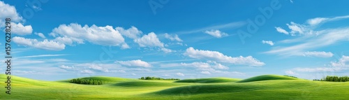 Green hills and meadow under blue sky with soft white clouds