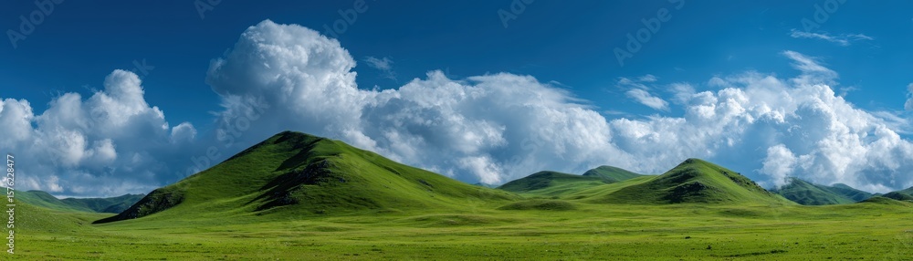 Obraz premium Green hills and meadow under blue sky with soft white clouds