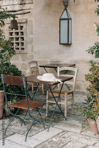 Fototapeta Naklejka Na Ścianę i Meble -  White feminine hat is on a table in a street cafe in an old european city