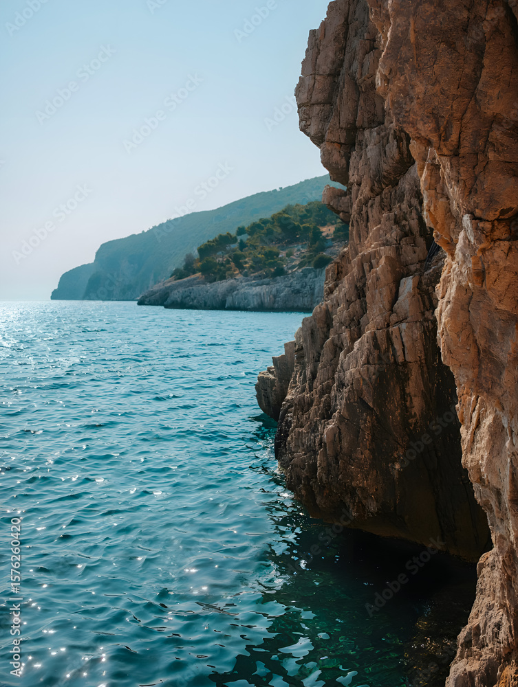 Naklejka premium Photo of sunlight sparkles on the turquoise sea water next to a rugged cliff face